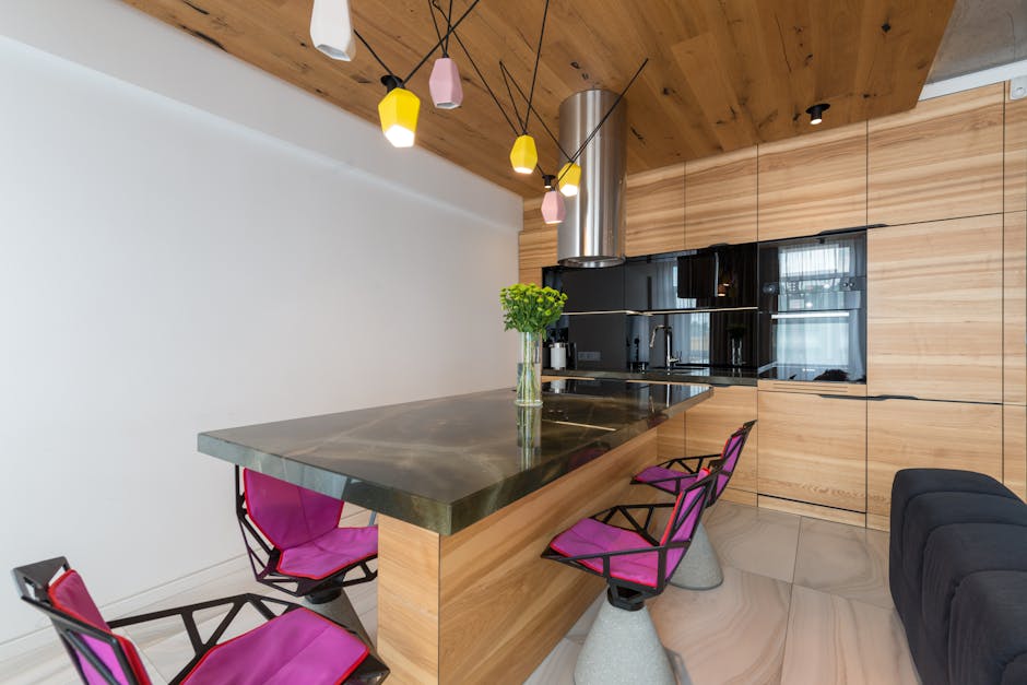 Stylish interior of contemporary kitchen with built in microwave and oven with stylish chairs around marble counter